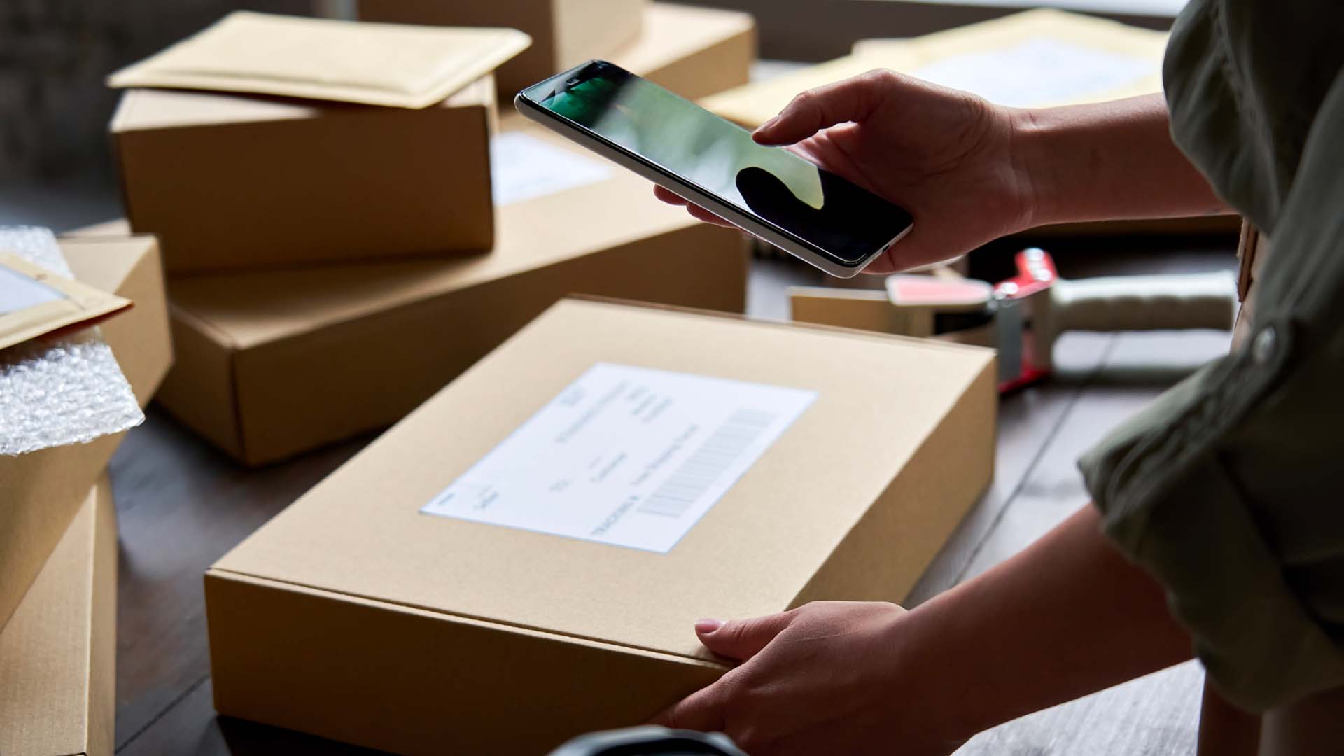 Persona gestionando un pedido desde un teléfono junto a paquetes de mercancía